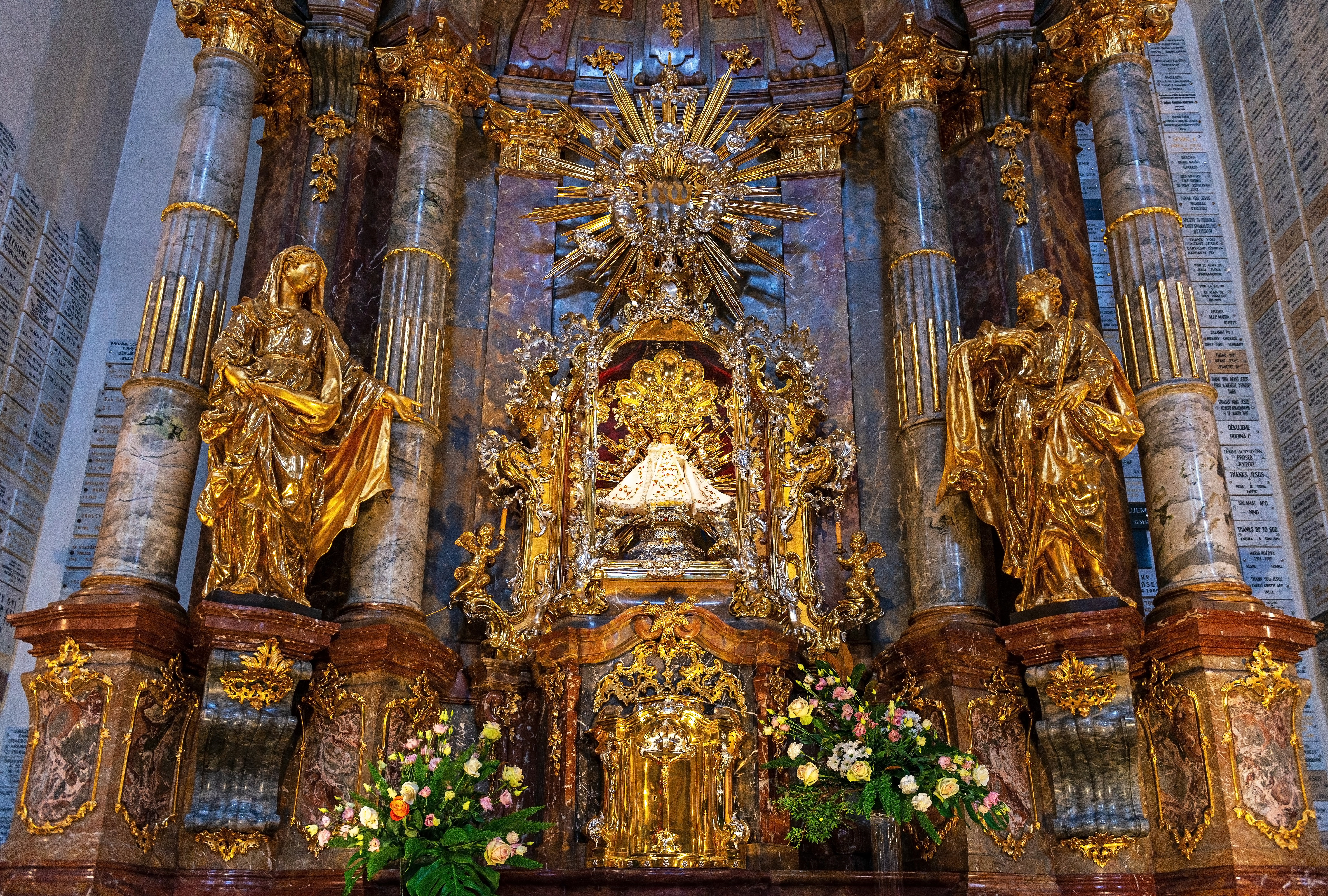 A small statue of an infant Jesus stands in the centre of a lavish, golden shrine in a church in Prague. The statue is wearing a white cloak.