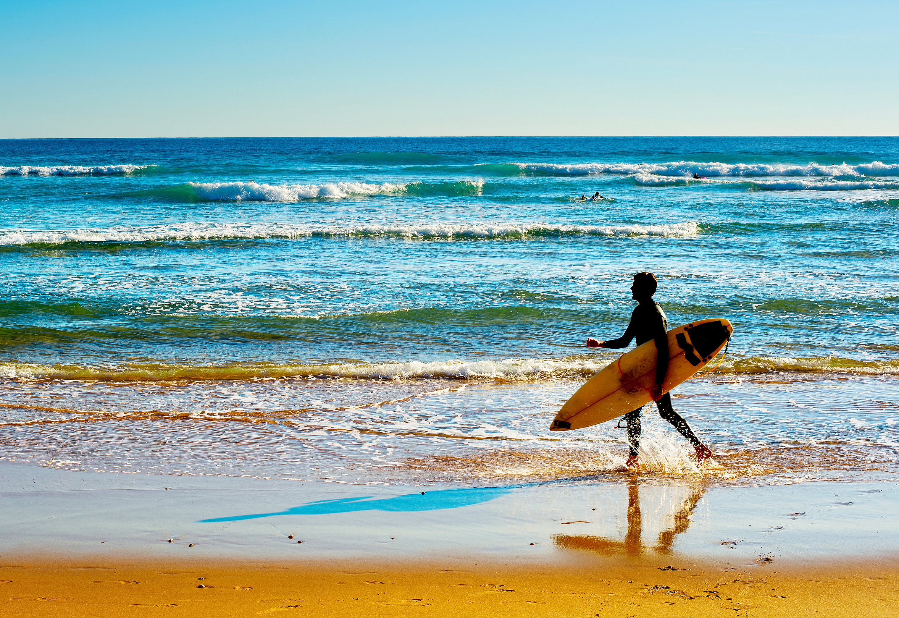 Surfer with surfboard walking on the beach in Portugal's Algarve