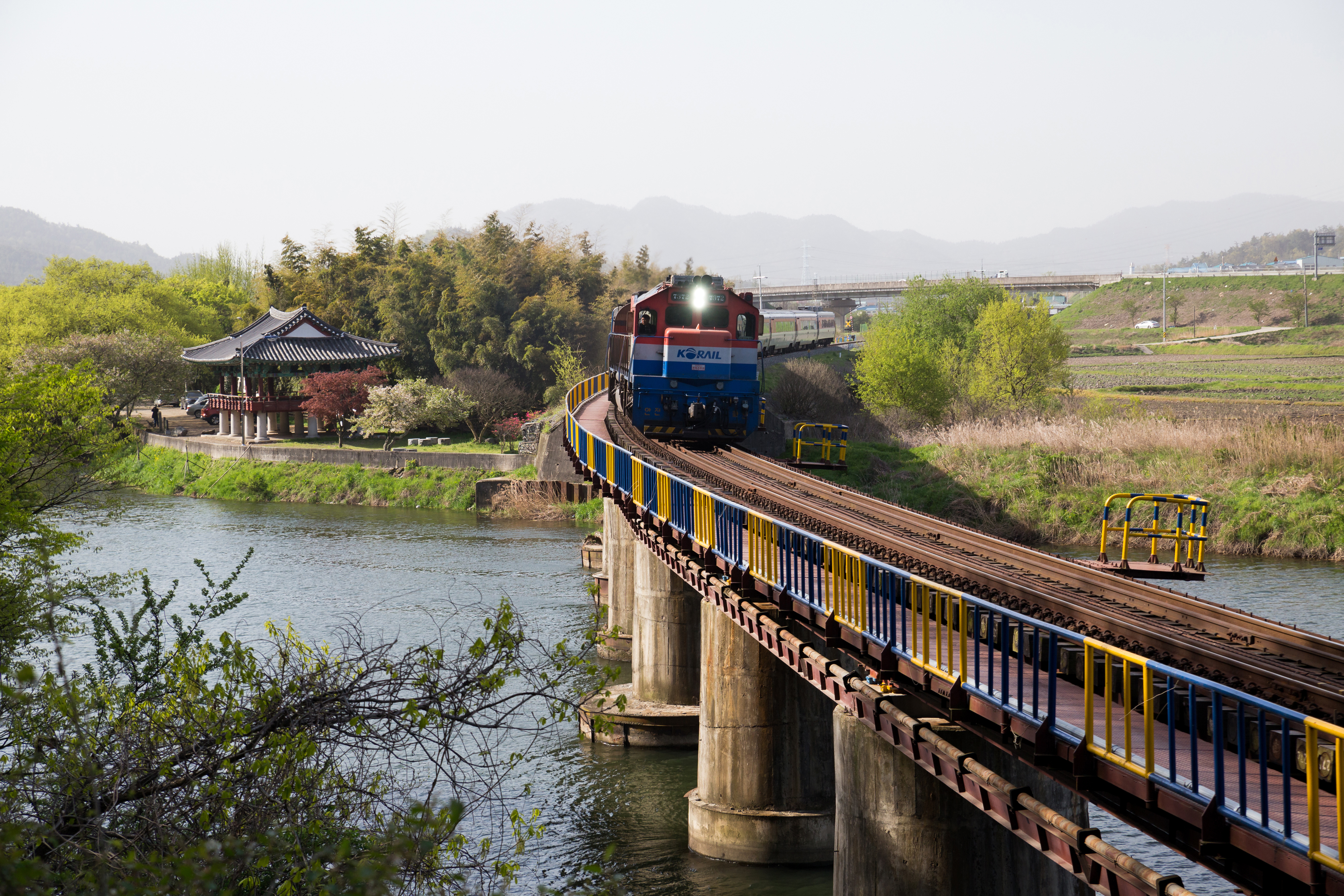 Morning view of Mugunghwa Train moving on railroad bridge on Jiseokcheon Stream with Yeongbyeokjeong Pavilion in the background