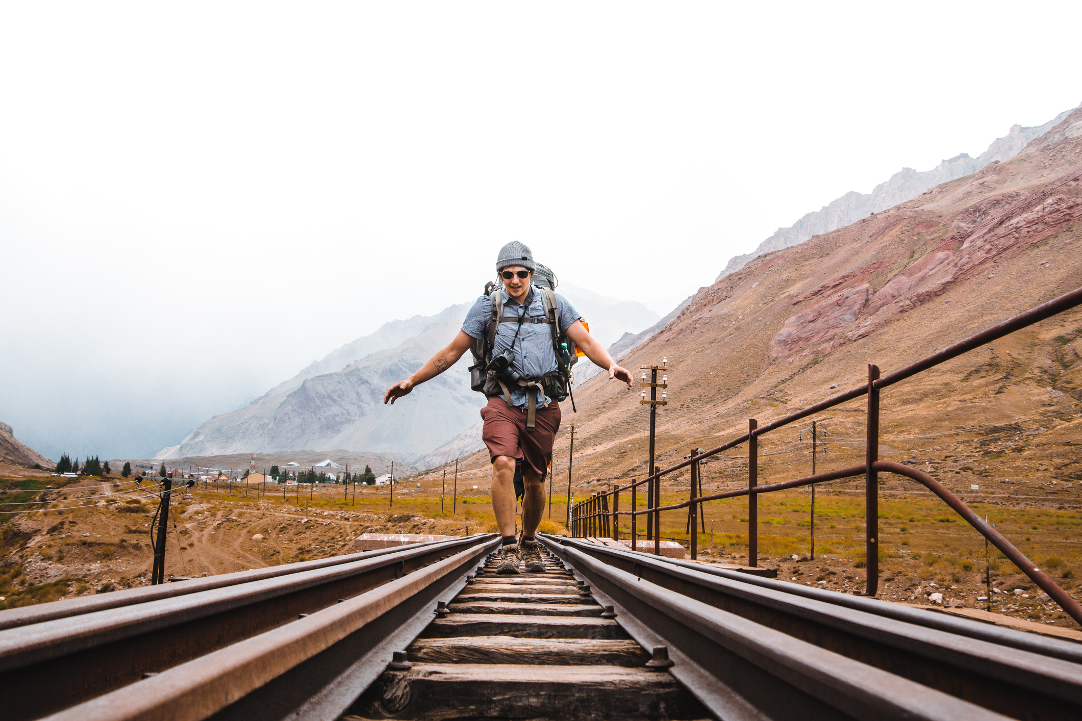 A man carrying hiking gear makes steps along an abandoned railway track in a mountainous area