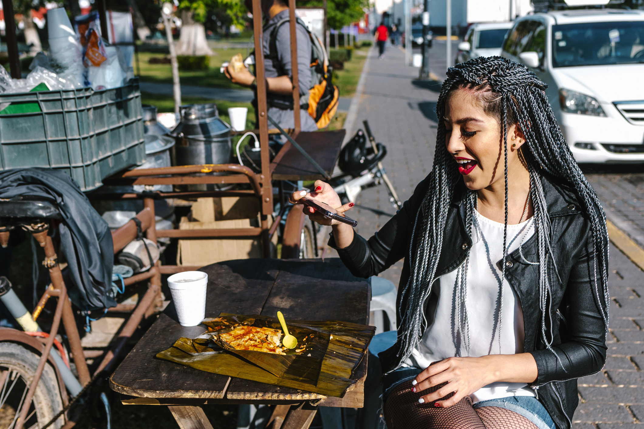 A woman takes a photo of her food that she's ordered from a nearby street-food trader