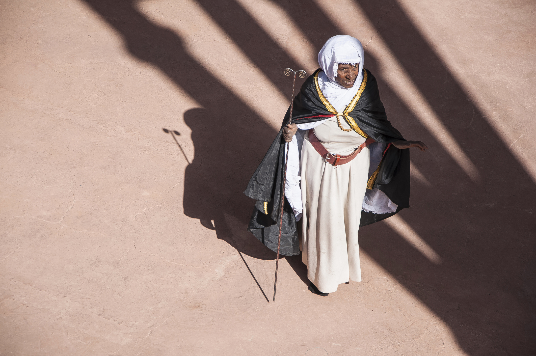 Senior African Christian woman in traditional dress casts a shadow under the sun