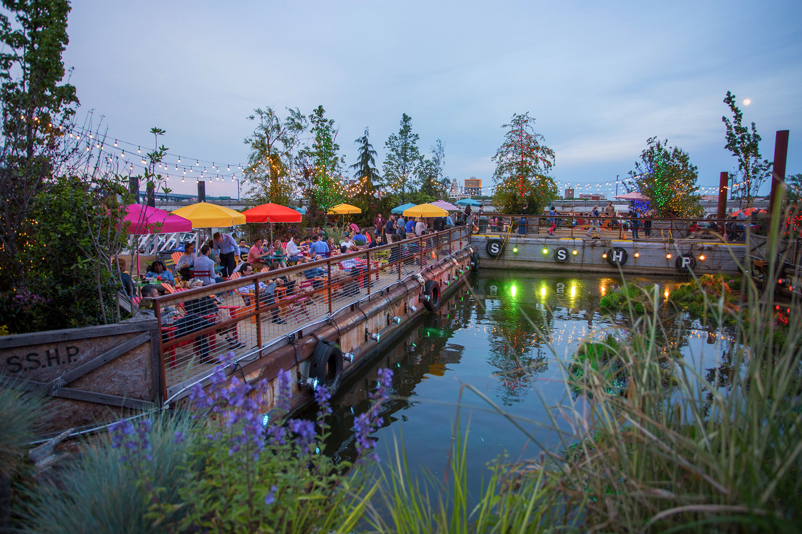 Long shot of park set up on docs on a river with red and yellow umbrellas over tables
